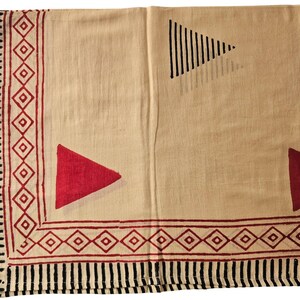 May include: A beige textile with a geometric design. The border features alternating black vertical lines and red diamond shapes. Red triangles and a black triangle with vertical lines are printed on the beige background.
