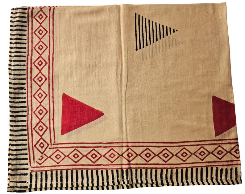 May include: A beige textile with a geometric design. The border features alternating black vertical lines and red diamond shapes. Red triangles and a black triangle with vertical lines are printed on the beige background.