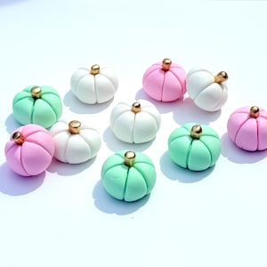 May include: A collection of small, decorative pumpkins in pastel colors: white, pink, and mint green. Each pumpkin has a gold-colored stem. These miniature pumpkins are likely used for crafting or seasonal decor.