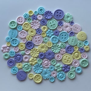 May include: A collection of pastel-colored buttons in various shapes and sizes, including round, square, and flower-shaped buttons. The buttons are made of a smooth, matte material and are perfect for crafting or decorating.