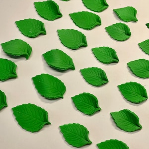 May include: A collection of 18 green fondant leaves, perfect for decorating cakes or cupcakes. The leaves are all the same size and shape, and they have a realistic texture.