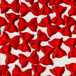 May include: A collection of red bow-shaped cake decorations. The bows are made of fondant or gum paste and are perfect for adding a festive touch to cakes, cupcakes, and other desserts.
