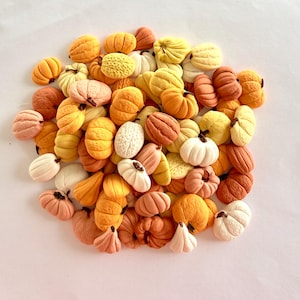 May include: A large collection of small, sculpted pumpkins in various shades of orange, yellow, white, and tan. Each miniature pumpkin features a textured, ribbed surface and a small, dark brown stem, arranged in a dense, overlapping pile.