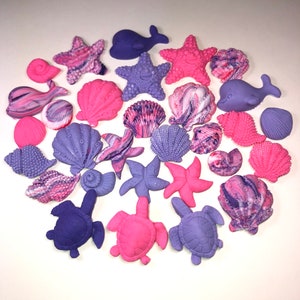May include: A collection of purple and pink sea-themed cake toppers, including seashells, starfish, turtles, and whales.