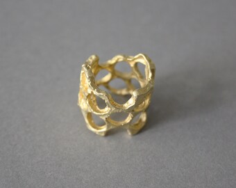 May include: A gold-colored ring with a unique, openwork design. The ring is made of a textured metal and has a honeycomb-like pattern.