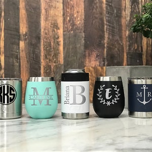 May include: Five stainless steel tumblers with different designs and personalized engravings. The tumblers are in various colors, including black, blue, and turquoise. The engravings include initials, names, and a nautical anchor.