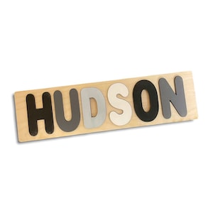 May include: Wooden puzzle with the name "HUDSON" spelled out in black, grey, and white letters.