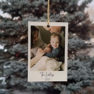 May include: A white card with a photograph of a family of three. The parents are holding a baby. The card has the text "The Lebtags 2023" printed on it.