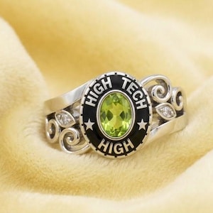 Pode incluir: Anel de prata com uma pedra preciosa verde oval no centro. O anel apresenta as palavras "HIGH TECH HIGH" em letras pretas ao redor da pedra preciosa. Redemoinhos decorativos e pequenas pedras transparentes adornam as laterais.