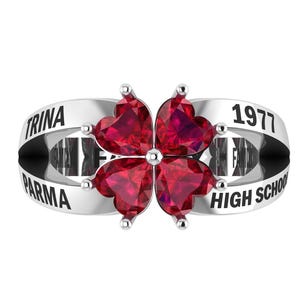 May include: A silver ring with four heart-shaped, deep red gemstones in a clover design. The ring band is engraved with the words "TRINA", "PARMA", "1977", and "HIGH SCHOOL".