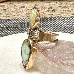 May include: A silver ring with a green and white gemstone, a clear gemstone, and a gold band.