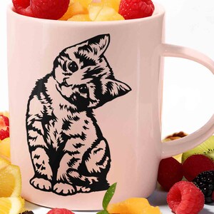 May include: A pink ceramic mug with a black silhouette of a kitten looking over its shoulder. The mug has a large handle and is decorated with a black and white kitten design.