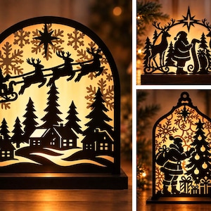 Op de afbeelding: Een set van drie boogvormige, zwarte, lasergesneden houten lichtdecoraties met verlichte silhouetten van de Kerstman, rendieren, dennenbomen, sneeuwvlokken en huisjes. Elk decoratief stuk is gemonteerd op een rechthoekige voet en geeft licht.