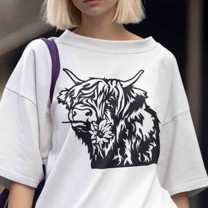 May include: White t-shirt with a black and white graphic of a Highland cow with a flower in its mouth.
