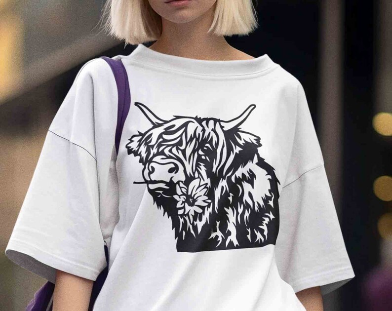 May include: White t-shirt with a black and white graphic of a Highland cow with a flower in its mouth.
