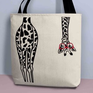 Pode incluir: Uma bolsa tote de lona branca com um design de girafa em preto e branco. A girafa est&aacute; usando &oacute;culos vermelhos e tem a cabe&ccedil;a de cabe&ccedil;a para baixo. As pernas da girafa s&atilde;o vis&iacute;veis no lado esquerdo da bolsa.