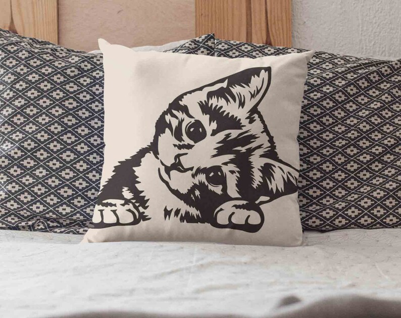 May include: A white pillow with a black and white illustration of a cat peeking out from the side. The cat has a striped pattern and is looking directly at the viewer.