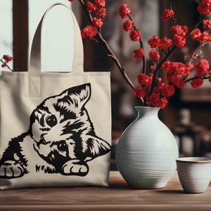 May include: A white canvas tote bag with black handles and a black and white illustration of a cat peeking out from the bottom of the bag.