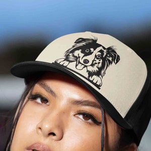 May include: A black and white border collie dog graphic on a beige and black trucker hat.