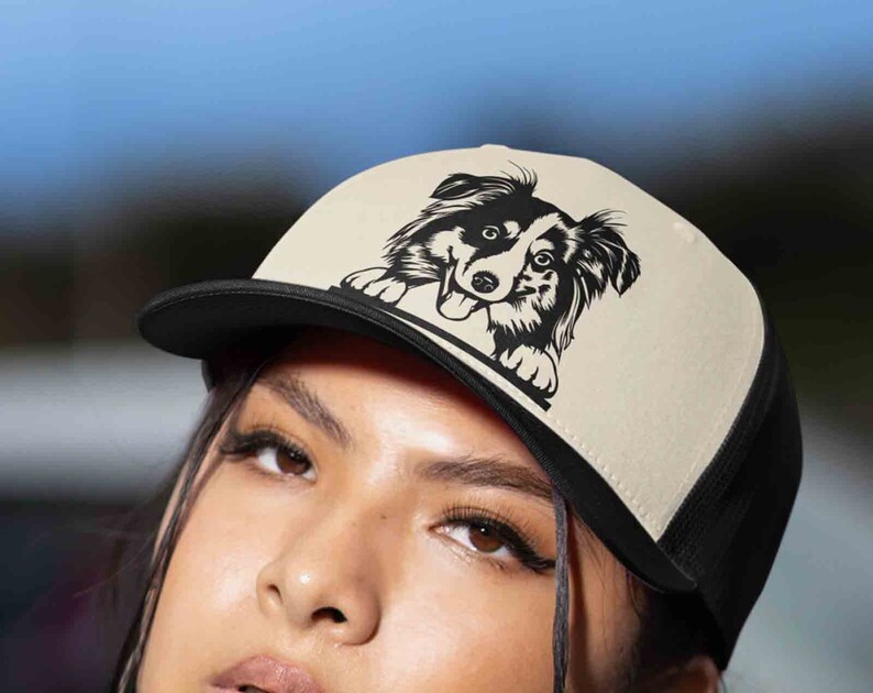 May include: A black and white border collie dog graphic on a beige and black trucker hat.