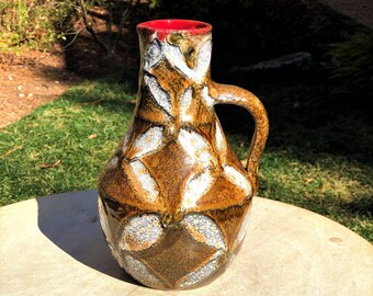 May include: A brown ceramic vase with a white and brown geometric pattern. The vase has a red rim and a handle.