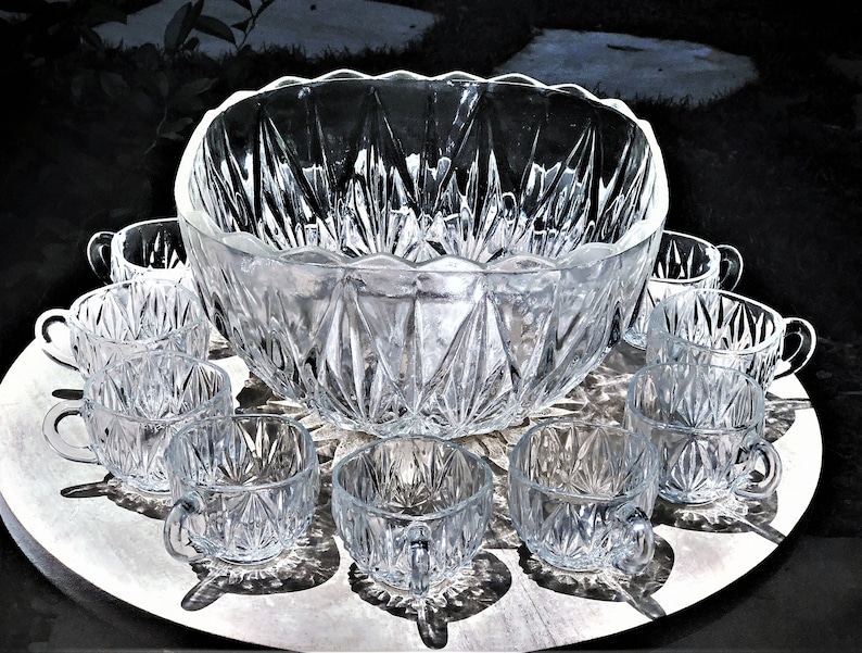 May include: A clear, cut-glass punch bowl set. The set includes a large bowl with a scalloped rim and several small cups. The glass has a diamond pattern, and the set is arranged on a silver tray.