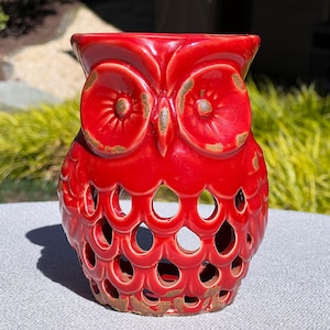 May include: Red ceramic owl candle holder with a cut-out design. The owl has a distressed finish and is perfect for adding a touch of whimsy to your home decor.