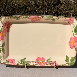 May include: Cream-coloured rectangular serving platter decorated with pink floral patterns and green leaves. The edges have a gold border. A gold-coloured metal handle is at the bottom.