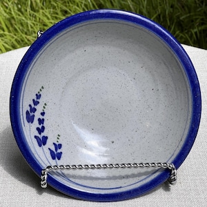 May include: A white ceramic bowl with a blue rim and a blue floral design. The bowl is on a white surface.