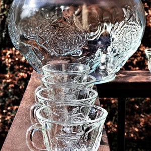 May include: A set of clear glass punch cups with a textured rose design. The cups are arranged in a row on a wooden surface.