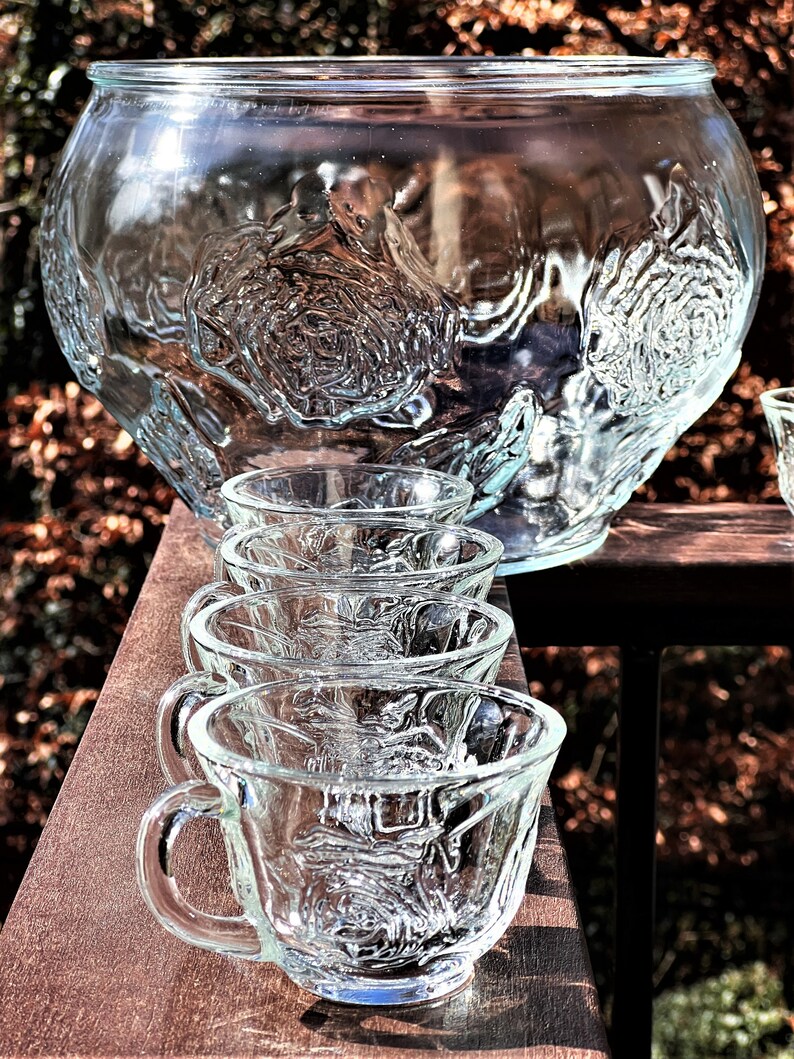May include: A set of clear glass punch cups with a textured rose design. The cups are arranged in a row on a wooden surface.