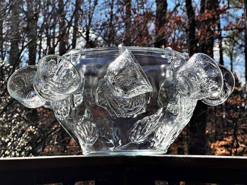May include: A clear glass punch bowl with a floral design and six matching cups hanging from the rim.