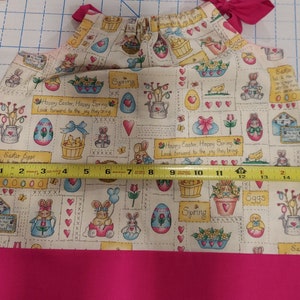 May include: A pink and white fabric with a repeating pattern of Easter eggs, bunnies, chicks, and flowers. The fabric has the text "Happy Easter, Happy Spring" and "Look forward to the joy they bring".