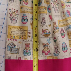 May include: A pink and white fabric with an Easter theme. The fabric features bunnies, eggs, baskets, and flowers. The fabric is 18 inches long.
