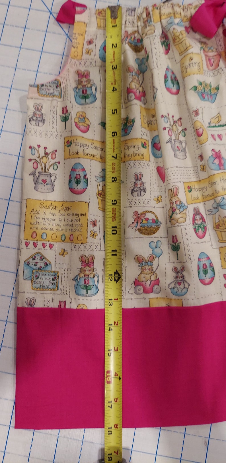 May include: A pink and white fabric with an Easter theme. The fabric features bunnies, eggs, baskets, and flowers. The fabric is 18 inches long.