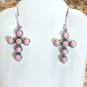 May include: A pair of silver cross earrings with pink stones. Each cross has seven stones.