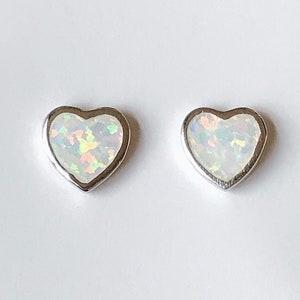 May include: A pair of silver heart-shaped earrings with white opal stones.