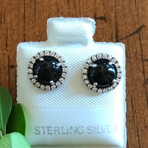 Può includere: Un paio di orecchini in onice nero con un alone d'argento di pietre di zircone cubico. Gli orecchini sono esposti su una carta bianca con il testo "STERLING SILVER".