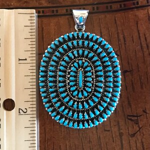 Pu&ograve; includere: Un ciondolo in turchese e argento con un design circolare. Il ciondolo ha un diametro di circa 5 cm e presenta un gruppo di pietre turchesi.