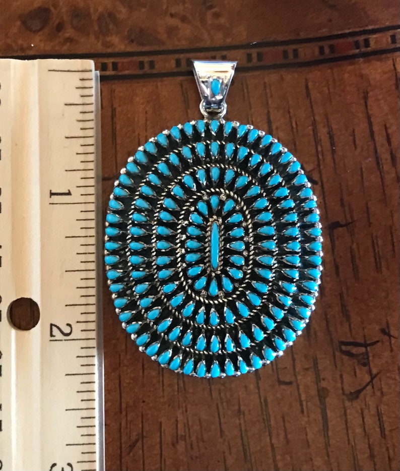 Pu&ograve; includere: Un ciondolo in turchese e argento con un design circolare. Il ciondolo ha un diametro di circa 5 cm e presenta un gruppo di pietre turchesi.