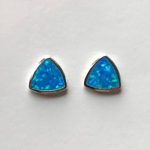 Puede incluir: Un par de pendientes de plata con una piedra de ópalo azul triangular en cada pendiente.