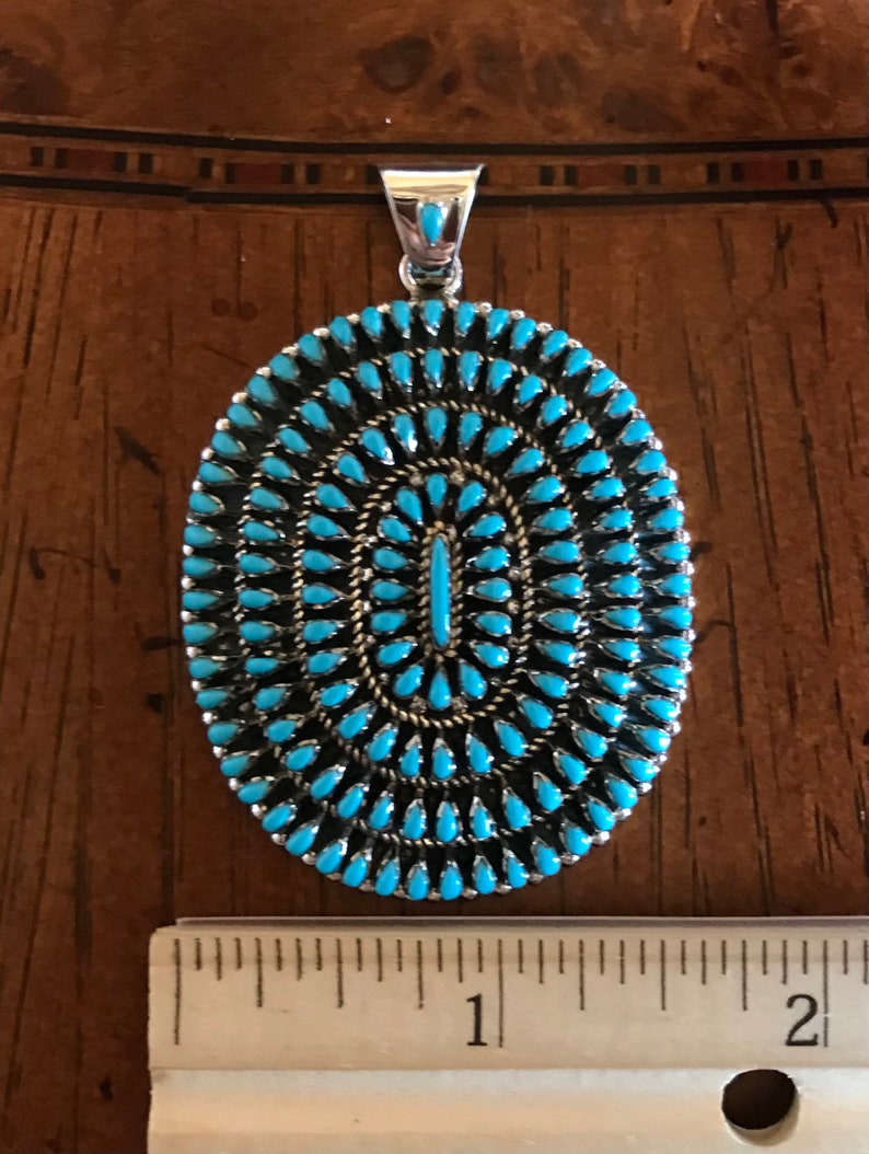Pu&ograve; includere: Un ciondolo in turchese e argento sterling con un gruppo di pietre turchesi di forma ovale. Il ciondolo misura circa 2,5 cm di diametro.