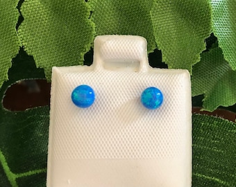 May include: A pair of blue opal stud earrings displayed on a white jewelry display card. The earrings are round and have a shimmery, iridescent finish.