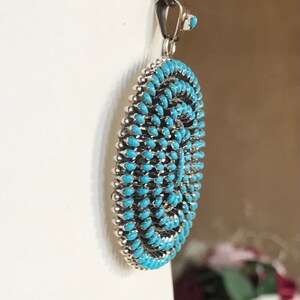 Pu&ograve; includere: Una collana con un ciondolo in turchese e argento. Il ciondolo &egrave; rotondo, piatto e ha un'intarsio in turchese. Il ciondolo &egrave; circondato da un bordo in argento.