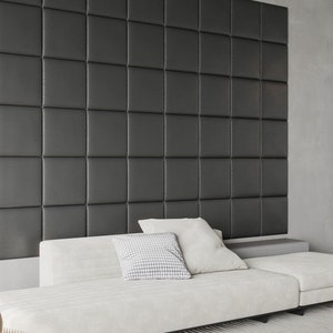 May include: A white sofa with two white pillows and one patterned pillow in front of a dark gray wall with square panels.
