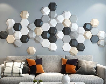 May include: A gray sofa with three pillows, two orange and one gray, sits in front of a wall decorated with 3D hexagonal tiles in shades of gray, white, and beige. A white coffee table with a gold metal decorative stand sits in front of the sofa.