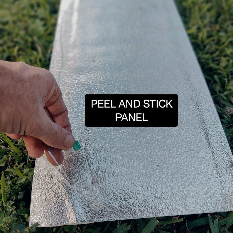 Pode incluir: Um painel prateado de descascar e colar com uma superf&iacute;cie texturizada. O painel tem uma aba verde na lateral e o texto "PEEL AND STICK PANEL" impresso nele.