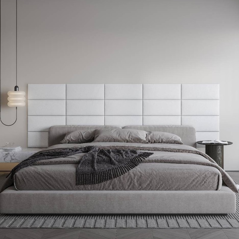 Pode incluir: Uma cama estofada cinza com uma cabeceira branca e um cobertor preto. A cama est&aacute; sobre um tapete cinza e h&aacute; uma pequena mesa de cabeceira preta ao lado da cama.