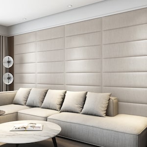 Pode incluir: Um sof&aacute; seccional branco com v&aacute;rias almofadas fica em frente a uma parede com pain&eacute;is estofados bege. O sof&aacute; est&aacute; em uma sala de estar com uma mesa de centro de m&aacute;rmore branco e um abajur com tr&ecirc;s c&uacute;pulas redondas de metal preto.