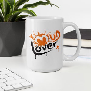 May include: White ceramic mug with a black and orange graphic that says "Mud Lover" with a heart shape and splattered paint design.